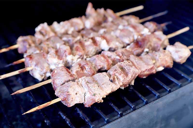 Horizontal image of grilling marinated cubed raw meat on a grill in a row.