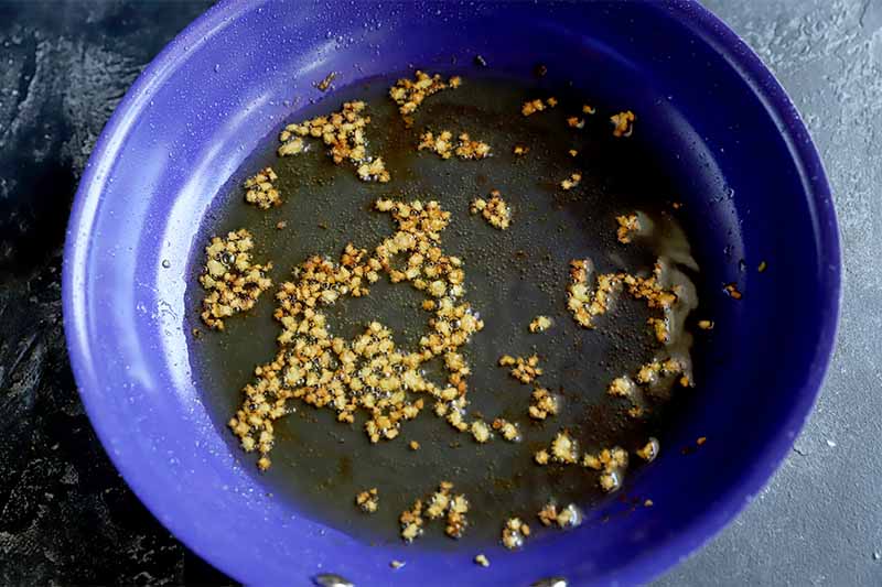 Horizontal image of a purple pan with a garlic and oil mixture.
