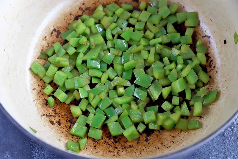 Horizontal image of cooking diced green peppers in a pot.