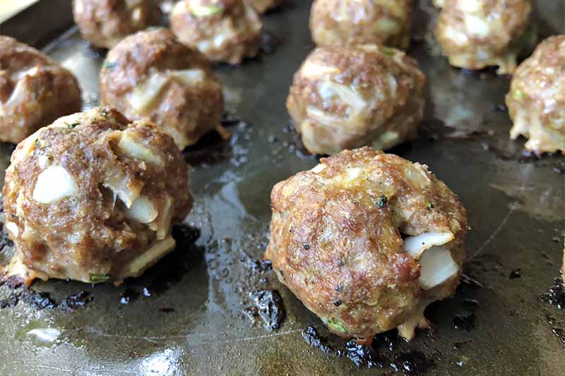 Horizontal image of baked meatballs in rows on a baking pan.
