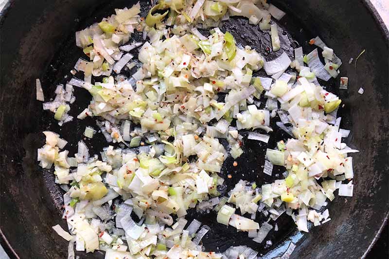 Horizontal image of cooked leeks and garlic in a cast iron skillet.
