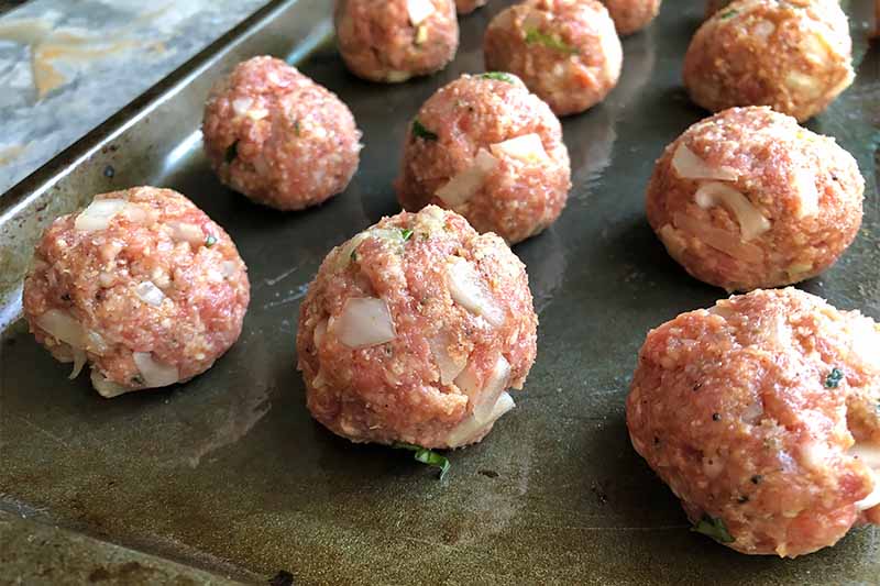 Horizontal image of raw meatballs on a greased baking pan.