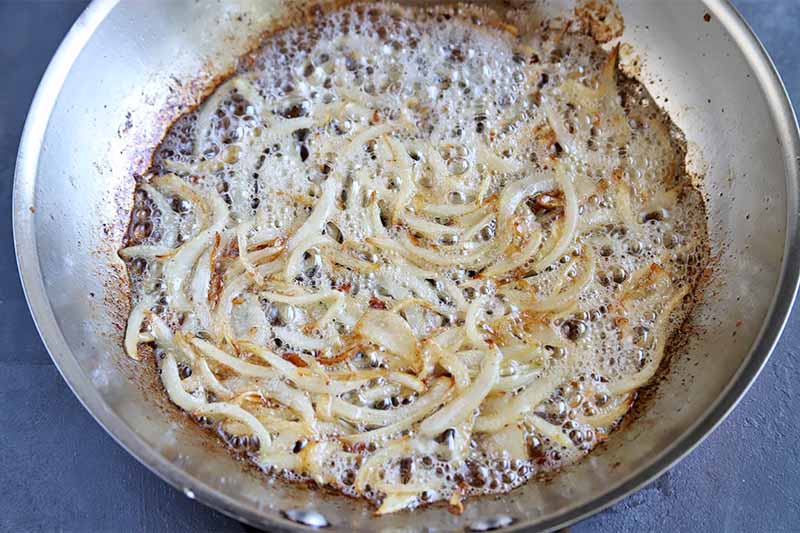 Horizontal image of lightly cooked sliced onions in a pan.