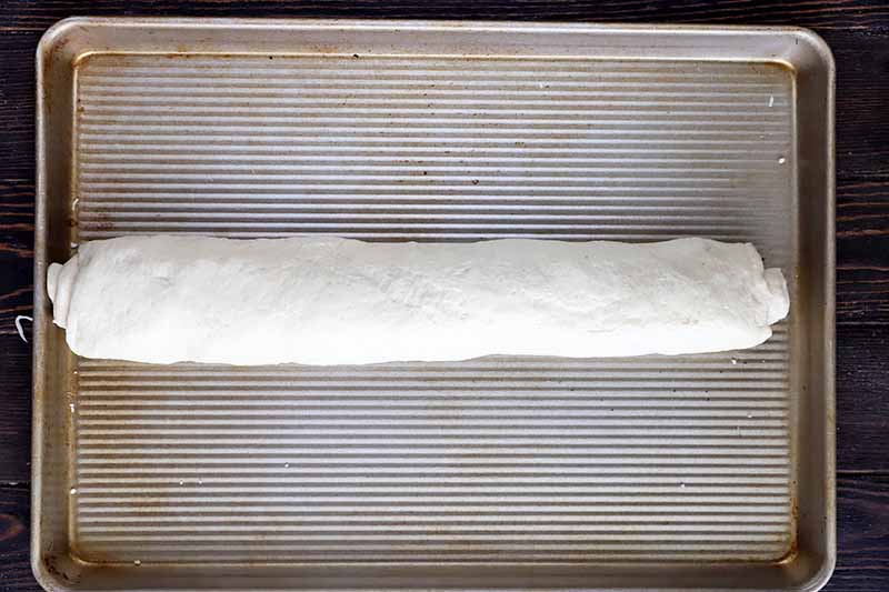 Horizontal image of a rolled log of dough on a baking sheet.