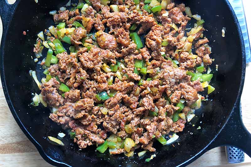 Horizontal image of a cast iron skillet with cooked crumbled sausage with onions and peppers.