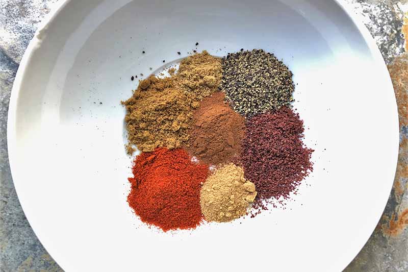 Horizontal image of divided mounds of spices in a white bowl.