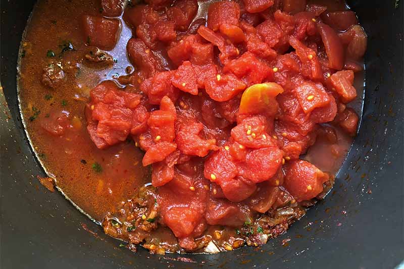Horizontal image of canned diced tomatoes in a spiced mixture in a pan.