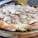 Horizontal image of a whole pizza topped with shingled thinly sliced potatoes.