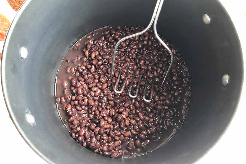 Horizontal image of mashing black beans in a large pot.
