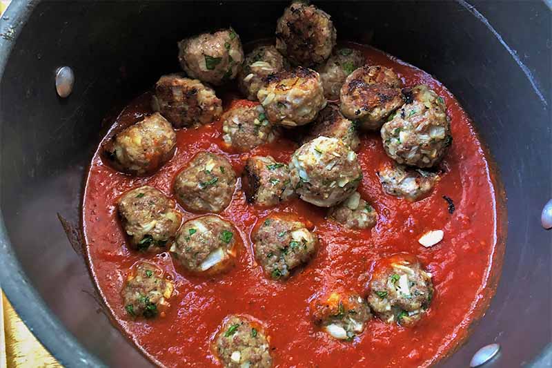 Horizontal image of mounds of cooked beef in a marinara sauce in a pot.