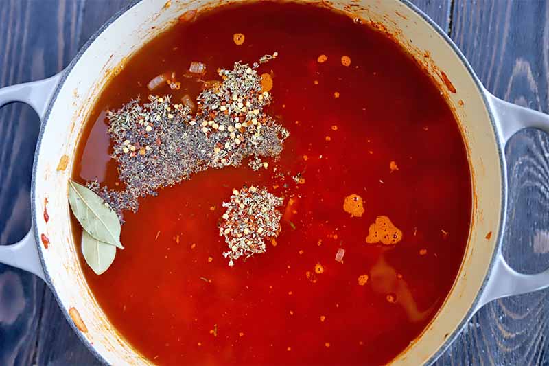 Horizontal image of a pot with tomato sauce and mounds of spices.