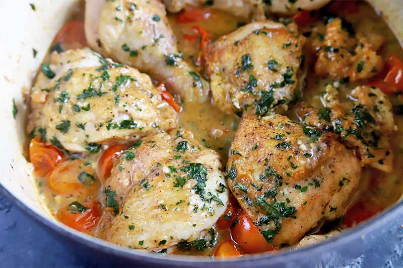 Horizontal image of a pot with a chicken dish with tomatoes and an herb white wine sauce.