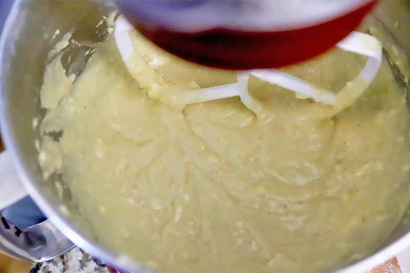 Horizontal image of a thick light yellow cake batter in the bowl of a stand mixer fitted with a paddle attachment.
