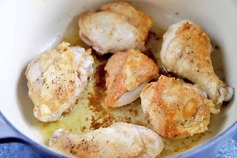 Horizontal image of searing poultry pieces in oil in a pot.