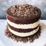 Horizontal image of a layered chocolate and vanilla cake on a cake stand with shaved chocolate.