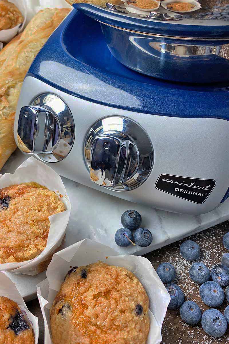 Vertical close-up image of the blue base of an appliance next to muffins and blueberries.