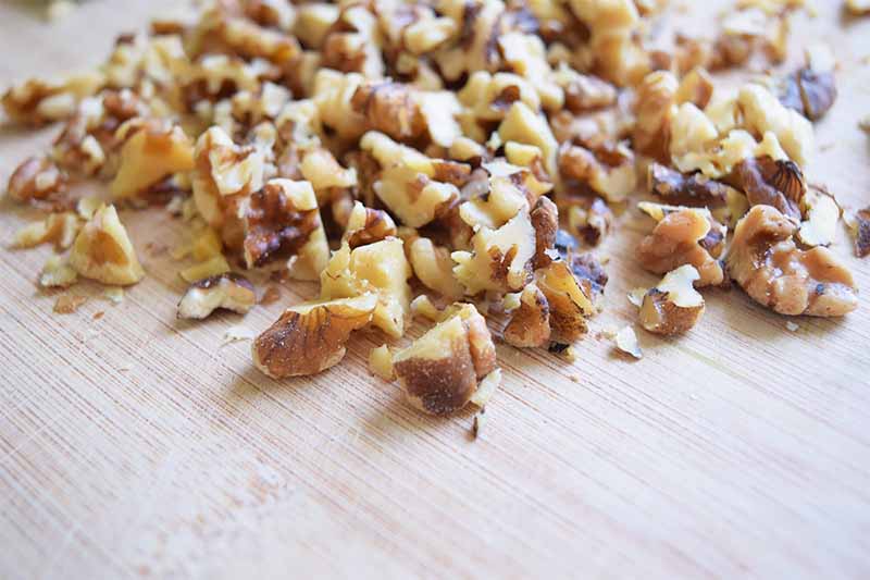 Horizontal image of chopped walnuts on a wooden cutting board.