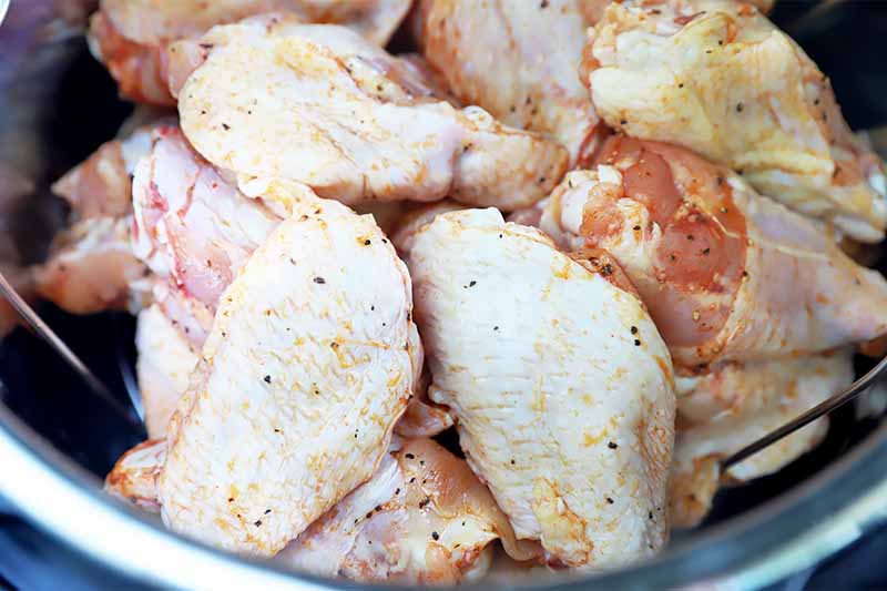Horizontal image of raw skin-on, bone-in poultry pieces with seasoning in a bowl.