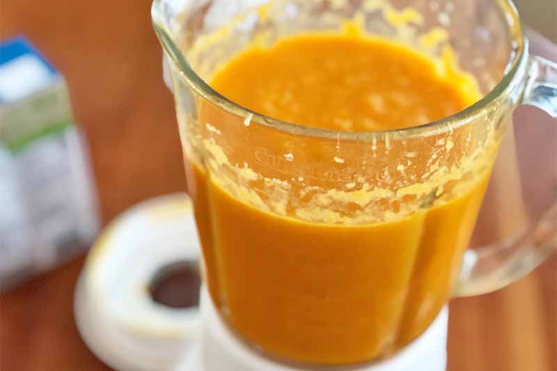 Horizontal image of a pureed orange mixture in a blender on a wooden table.