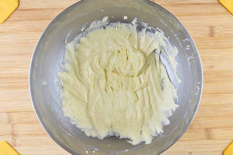 Horizontal image of a light yellow batter in a metal bowl on a wooden cutting board.