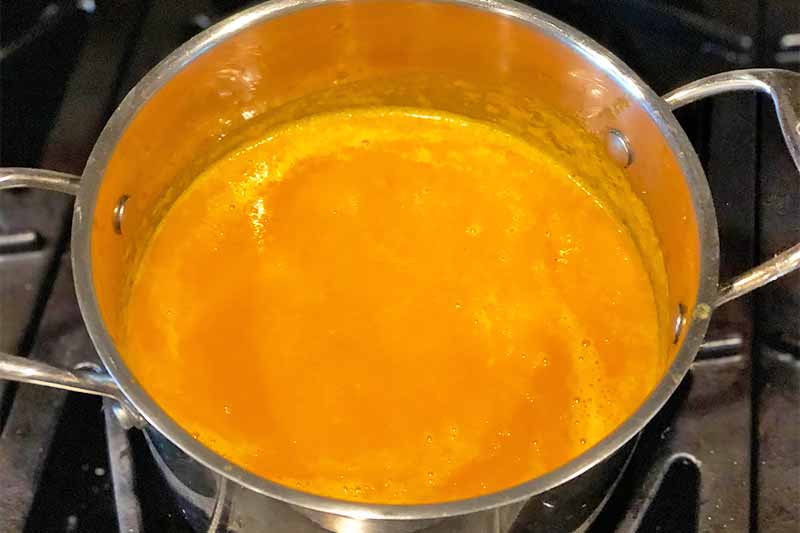 Horizontal image of a large pot filled with a bright orange pureed mixture on the stovetop.