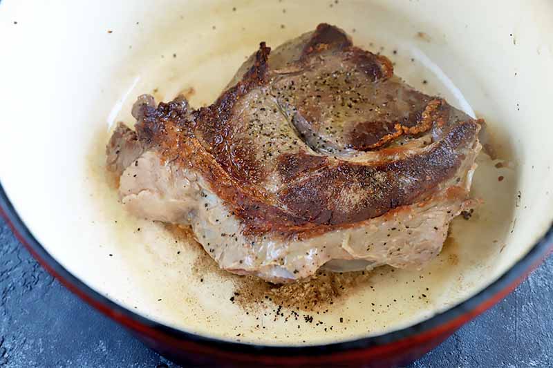 Horizontal image of a large piece of seared meat in a pot.