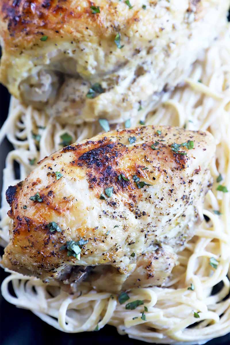Vertical image of two pieces of cooked and spiced poultry on top of spaghetti in a cream sauce.