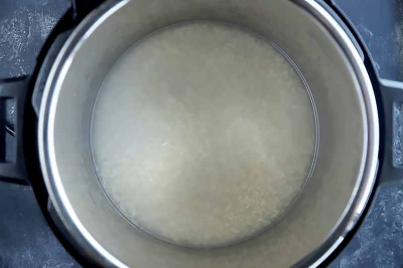Horizontal image of a metal bowl filled with water and white grains.