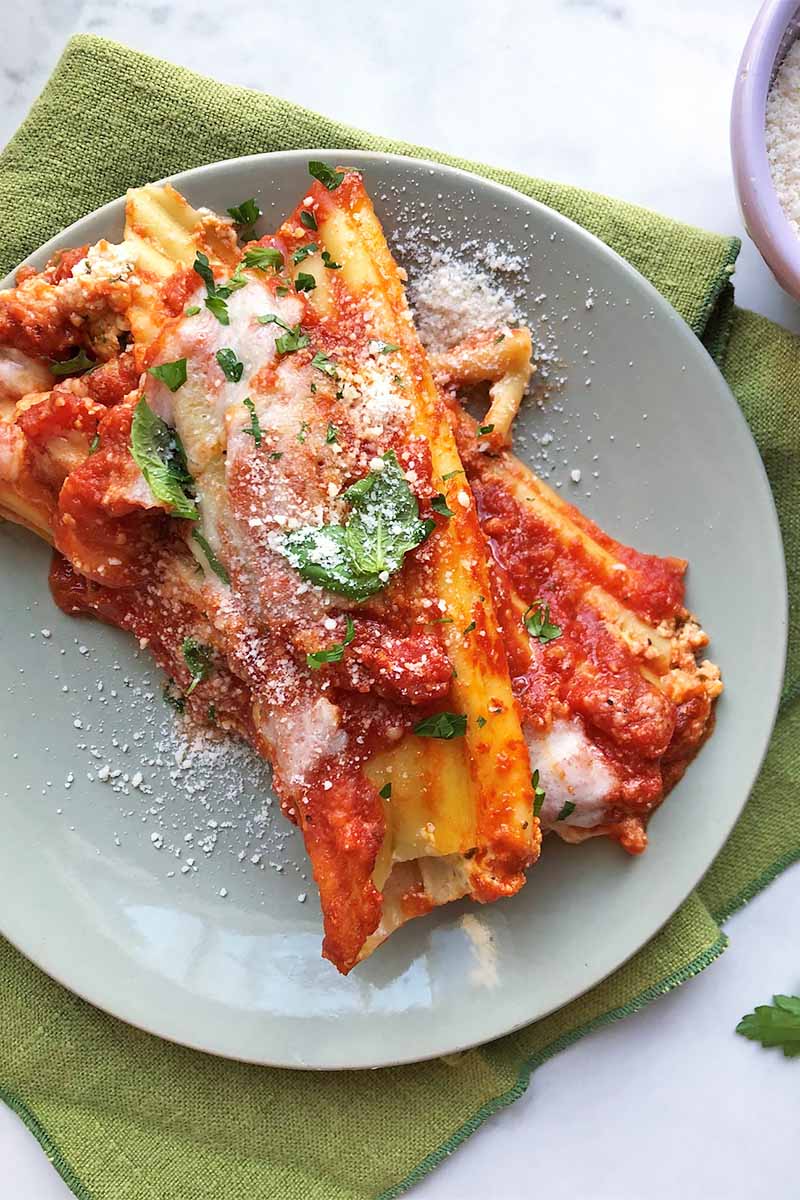 Vertical close-up top-down image of a plate with stuffed shells topped with marinara, grated parmesan, and fresh herbs.