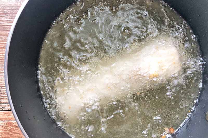 Horizontal image of frying a large burrito in bubbling oil in a pot.