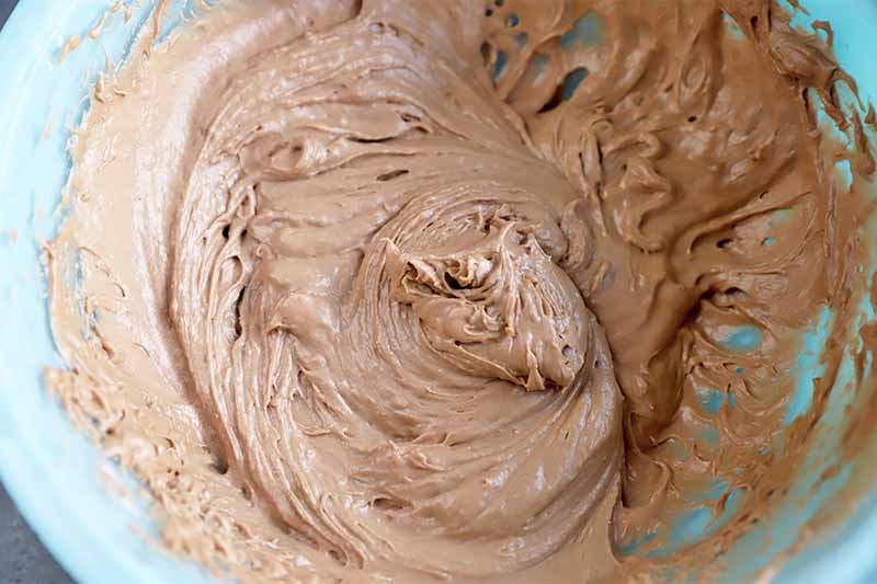 Horizontal image of a fluffy brown icing in a blue bowl.