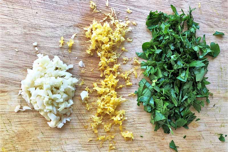 Horizontal image of finely chopped alliums and parsley, and grated lemon zest