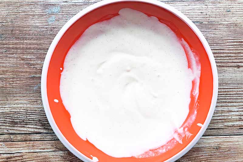 Horizontal image of a red bowl full of a mayonnaise mixture.