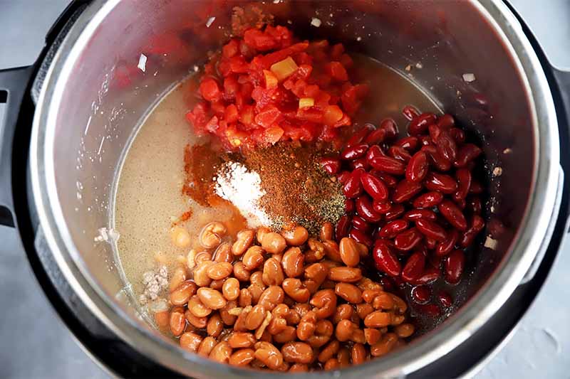Horizontal image of a pot filled with mounds of beans, tomatoes, and seasonings.