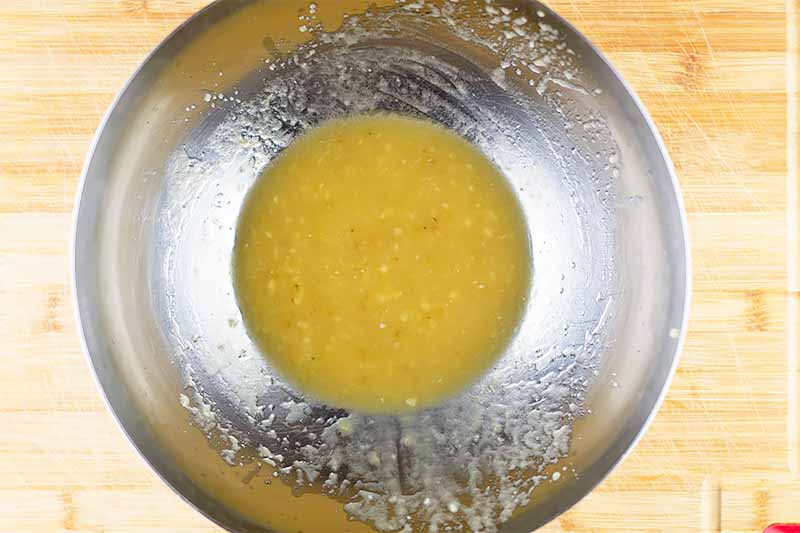 Horizontal image of a metal bowl filled with a lightly chunky yellow liquid mixture.