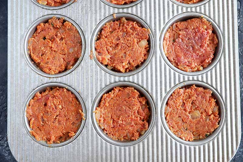 Horizontal image of a muffin pan filled with a seasoned ground beef mixture.