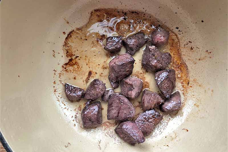Horizontal image of searing chunks of meat in a pot.