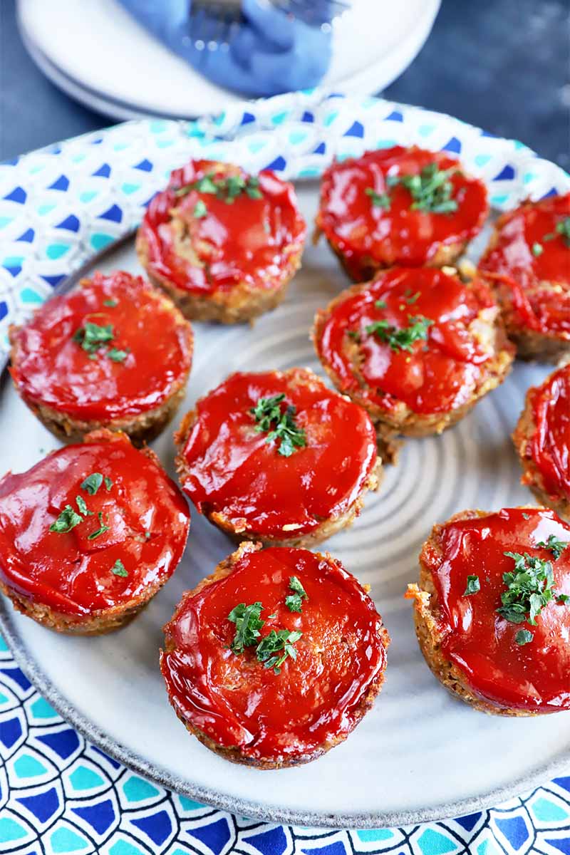 Vertical image of a white plate with scattered individual portions of ketchup-topped round appetizers.
