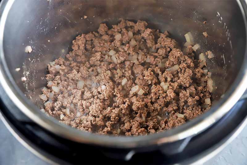 Horizontal image of cooking ground meat and chopped onions in a pot.