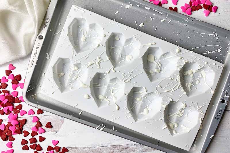 Horizontal image of scattered splatters of white melted candies in a silicone mold on a baking sheet.