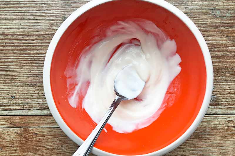 Horizontal image of a spoon mixing a thick white mixture in a red bowl.
