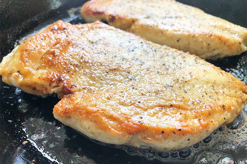 Horizontal image of seared poultry breasts in a cast iron skillet.