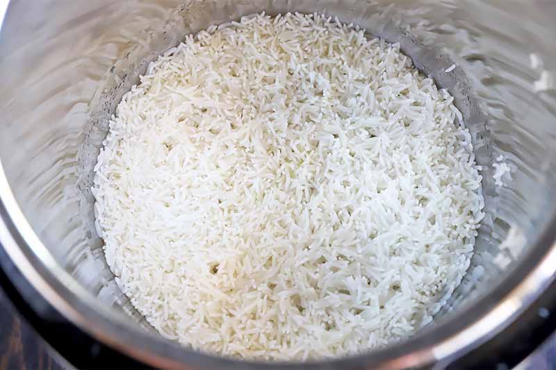 Horizontal image of a metal bowl full of cooked white grains stuck together tightly.