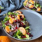 Horizontal image of a salad with citrus segments on a gray plate surrounded by whole citrus fruit.