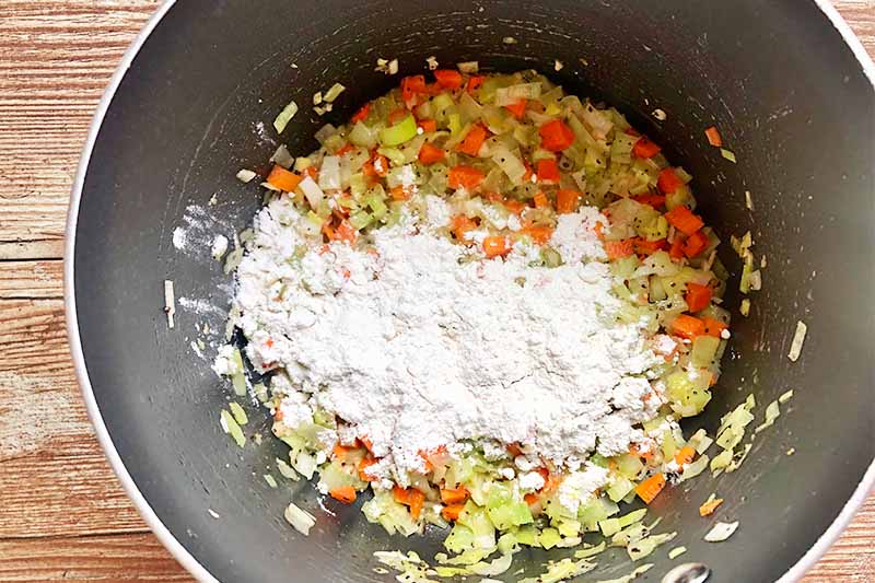 Horizontal image of flour sprinkled over chopped and cooked vegetables in a pot.