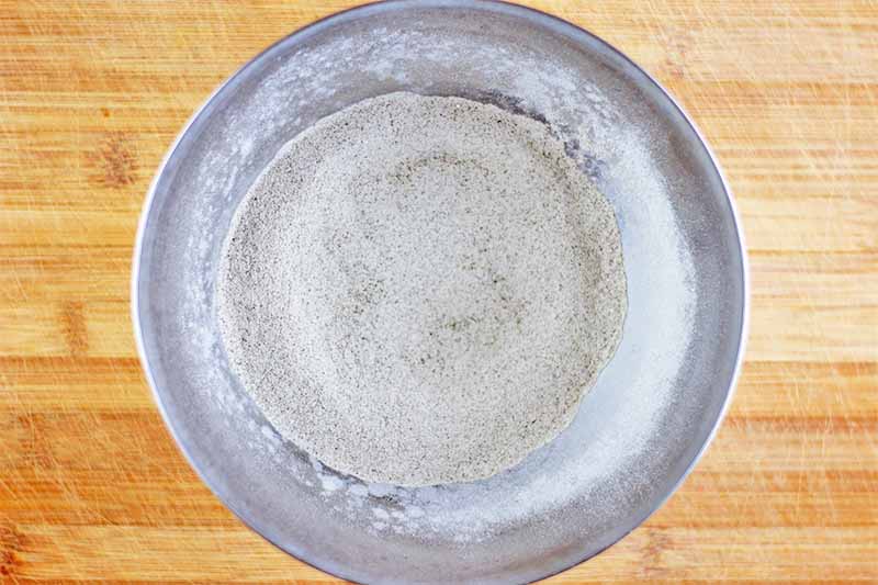 Horizontal image of a mix of dry flours in a metal bowl on a wooden surface.