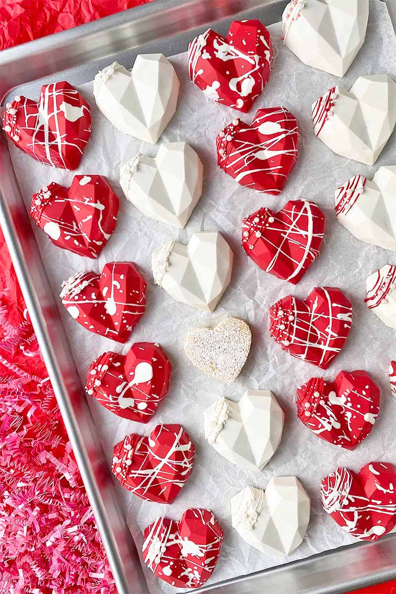 Vertical top-down image of neat rows of decorated red and white candies on a sheet pan lined with parchment paper.