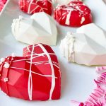 Horizontal image of decorated red and white chocolate shells on a white plate next to pink confetti.