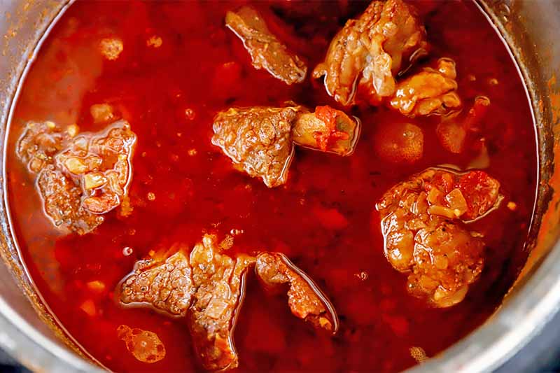 Horizontal image of cooked chunks of meat in a red liquid in a bowl.