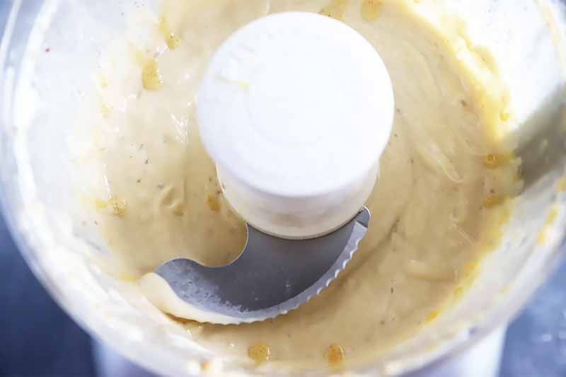 Horizontal image of a food processor with a creamy white mixture inside.